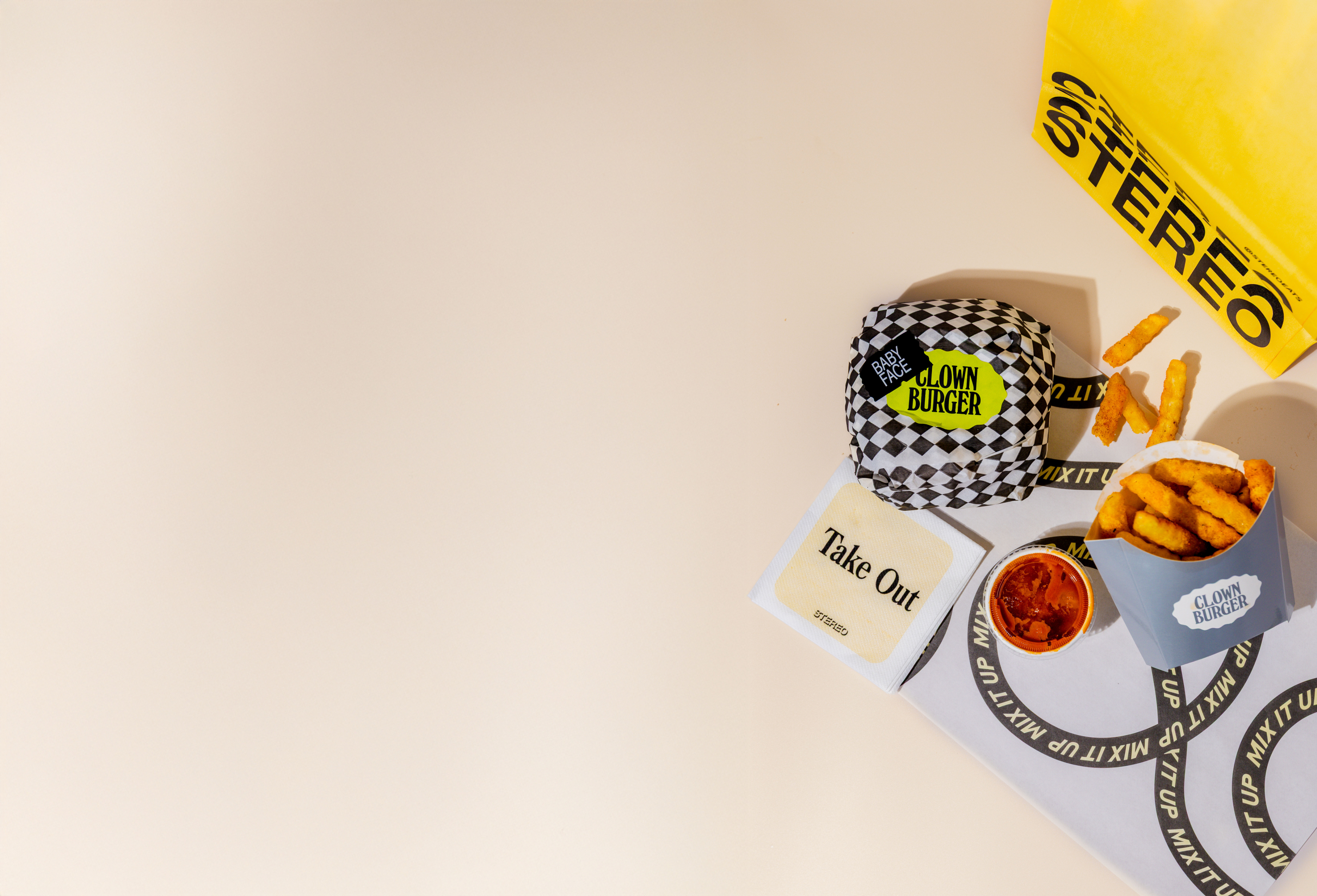 Clown Burger packaging with fries and a drink on a beige background